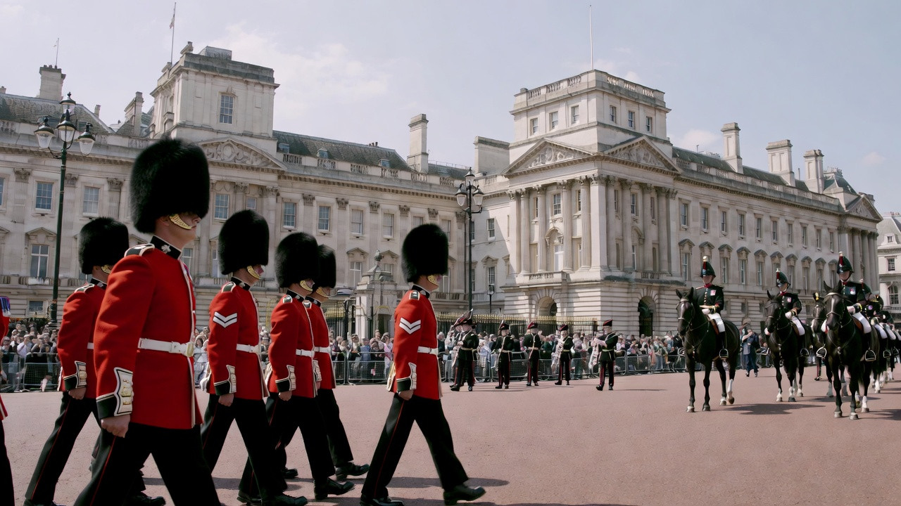 Scène vivante de la Relève de la Garde à Buckingham Palace, Londres, avec gardes en uniformes rouges et chapeaux en fourrure d’ours, fanfare militaire, foule de visiteurs et ciel bleu.